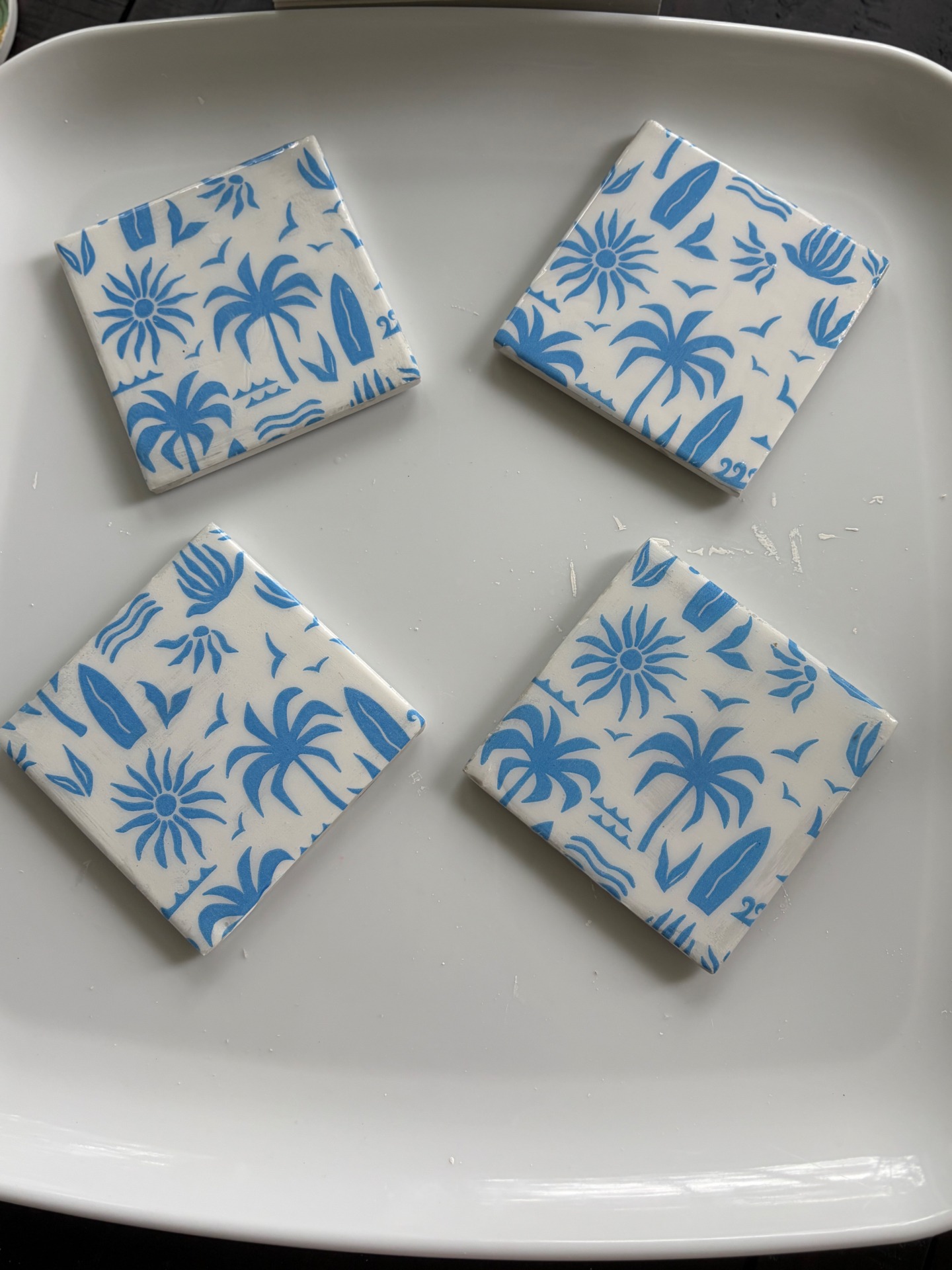 Four hand-decoupaged stone coasters with blue palm trees, surfboards, and sunbursts.