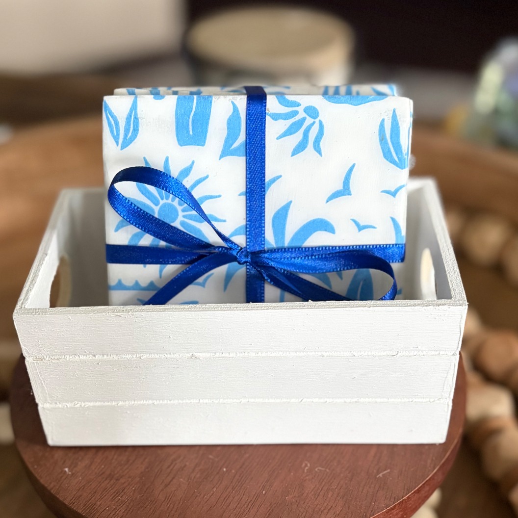 Blue palm and surf coaster set tied with royal blue ribbon in a whitewashed wooden crate.