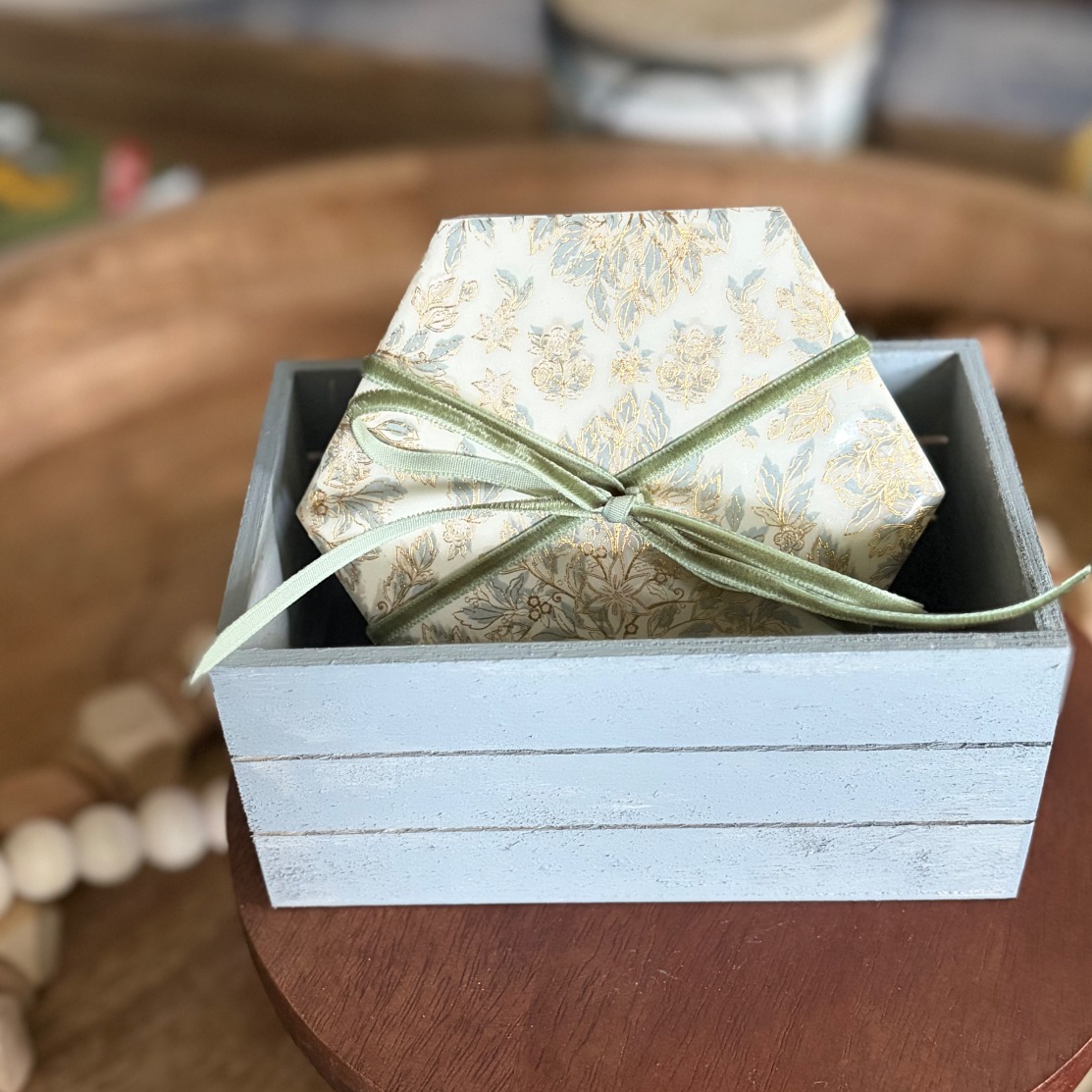 Gift-ready set of gilded hexagonal coasters tied with a sage velvet ribbon in a pale blue crate.