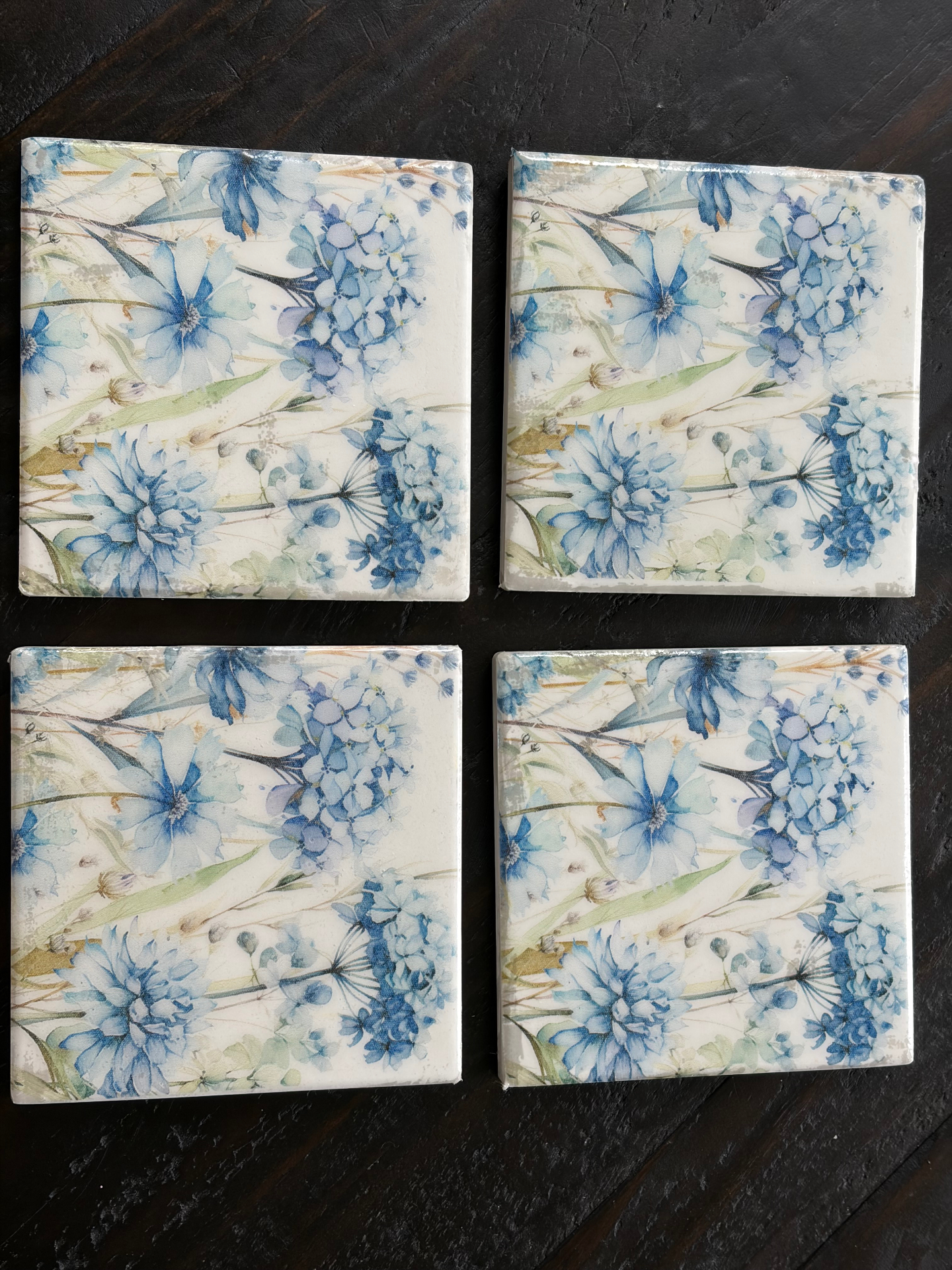 Four hand-decoupaged stone coasters with a soft blue hydrangea and wildflower print.
