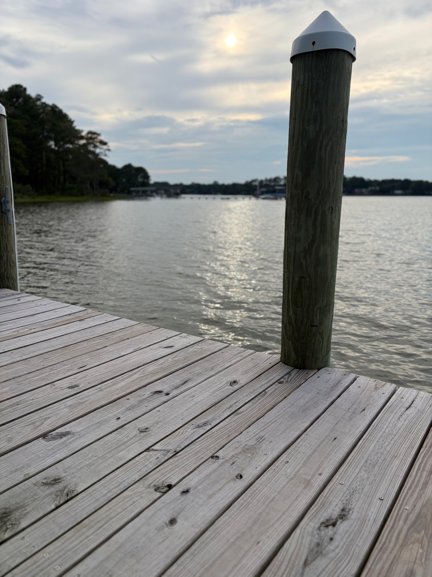 Wooden dock stretching out over the Chesapeake Bay at golden hour, weathered planks in the foreground and a piling silhouetted against the water.