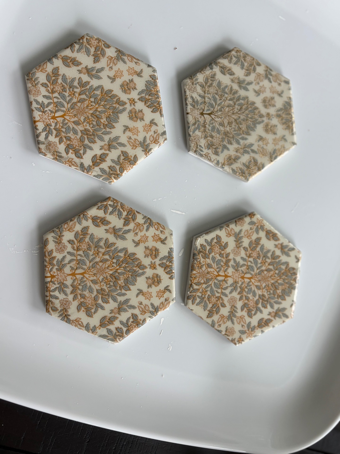 Set of four hexagonal coasters with a delicate gold and soft sage botanical pattern.