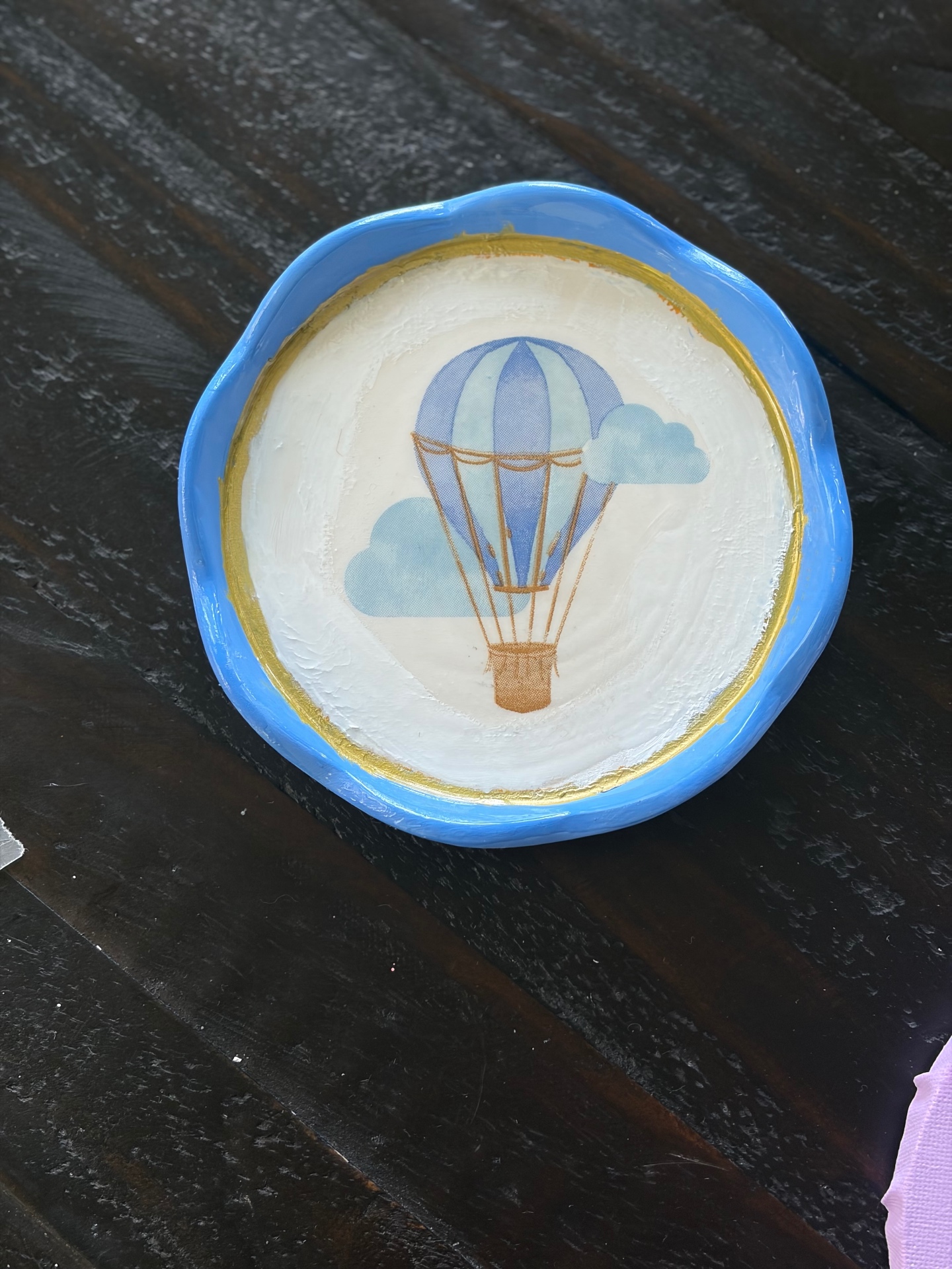 Small round trinket dish with a bright blue rim, gold inner ring, and a hot air balloon and clouds decoupaged in the center.