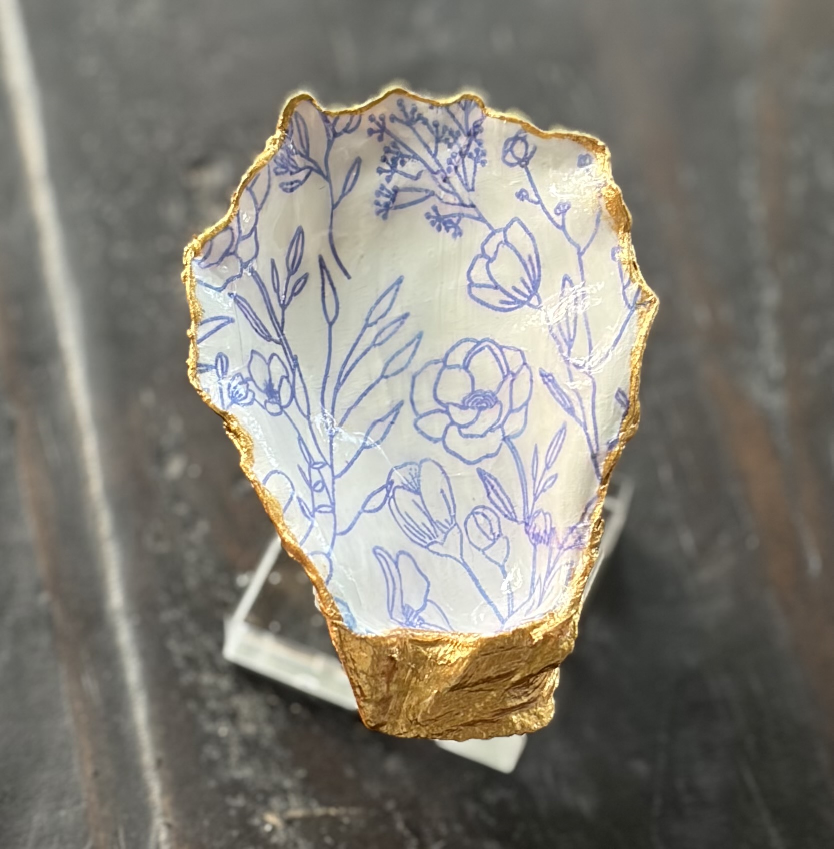 Oyster-shell trinket dish with hand-painted blue florals and a gold-leaf rim.