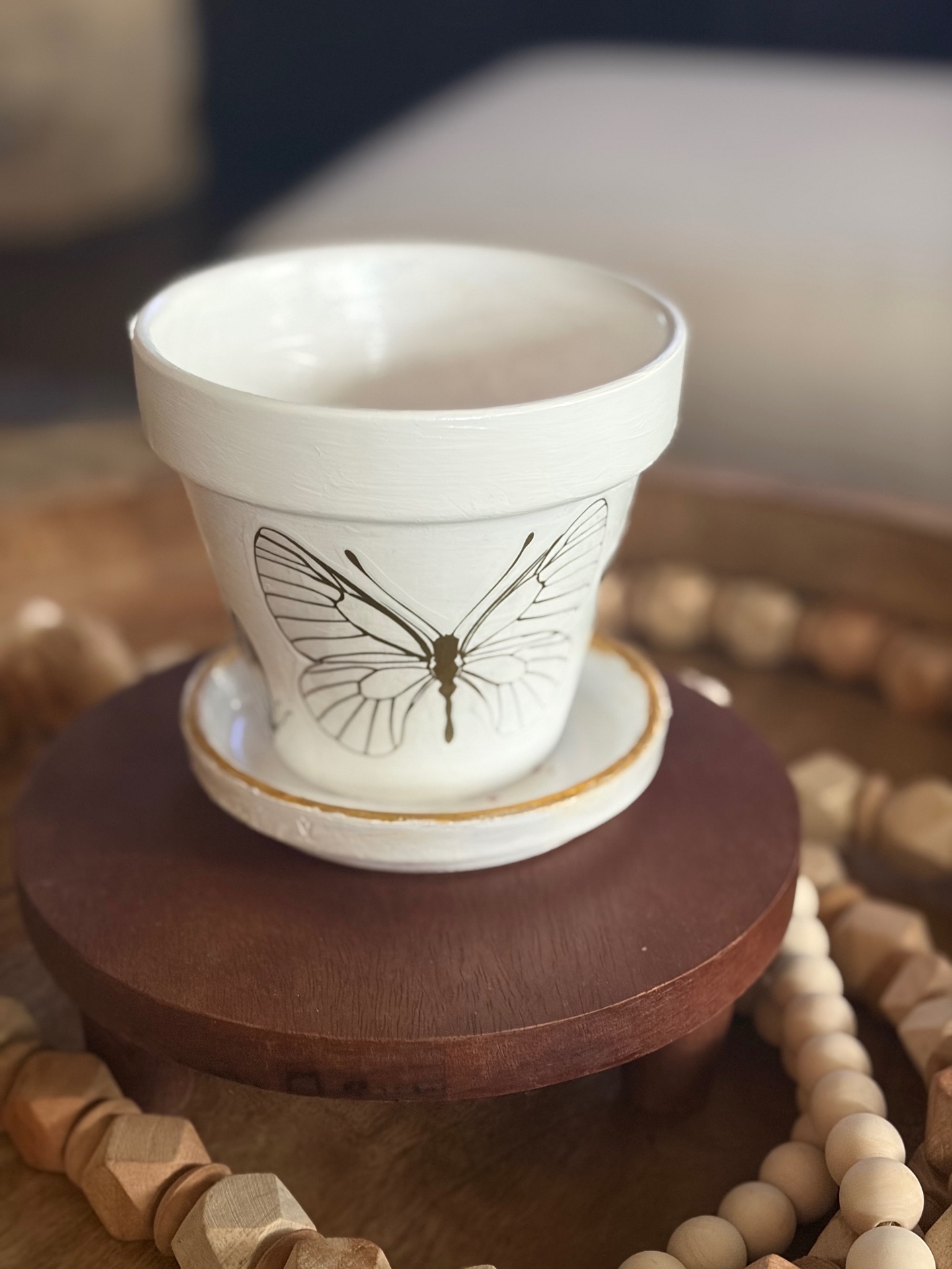 Small white terracotta planter with a delicate black butterfly transfer on the front, sitting on its matching saucer.